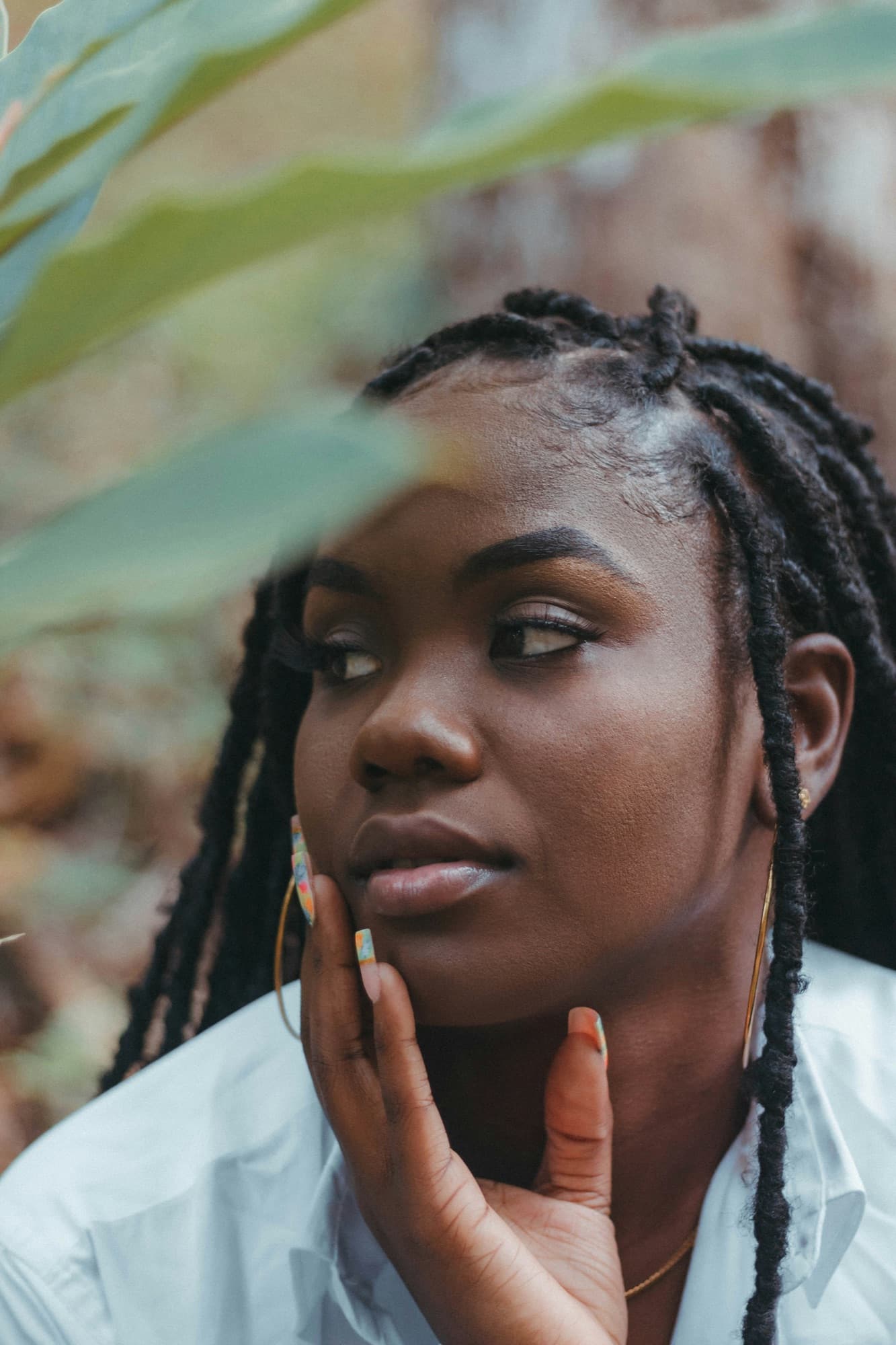 Femme aux locks et aux ongles vernis, la main sur la joue